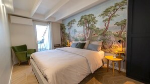 Une chambre à coucher avec un grand lit, un fauteuil vert, une petite table avec une lampe et une fresque murale.