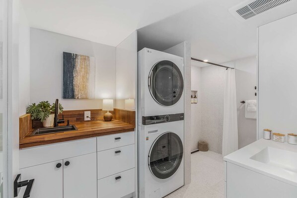 A modern bathroom with a double washer-dryer unit, a wooden vanity with a sink, and a large mirror.