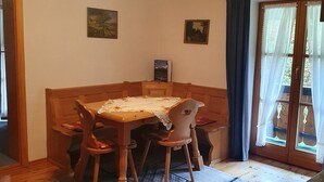 Ruokailutila, jossa on puinen pöytä ja tuolit, kattovalaisin ja näkymä lasiovesta.
