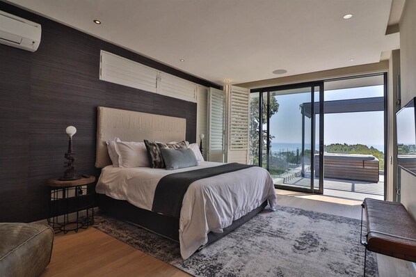 A modern bedroom with a large bed, a nightstand, and a view of the outdoors through a sliding glass door.