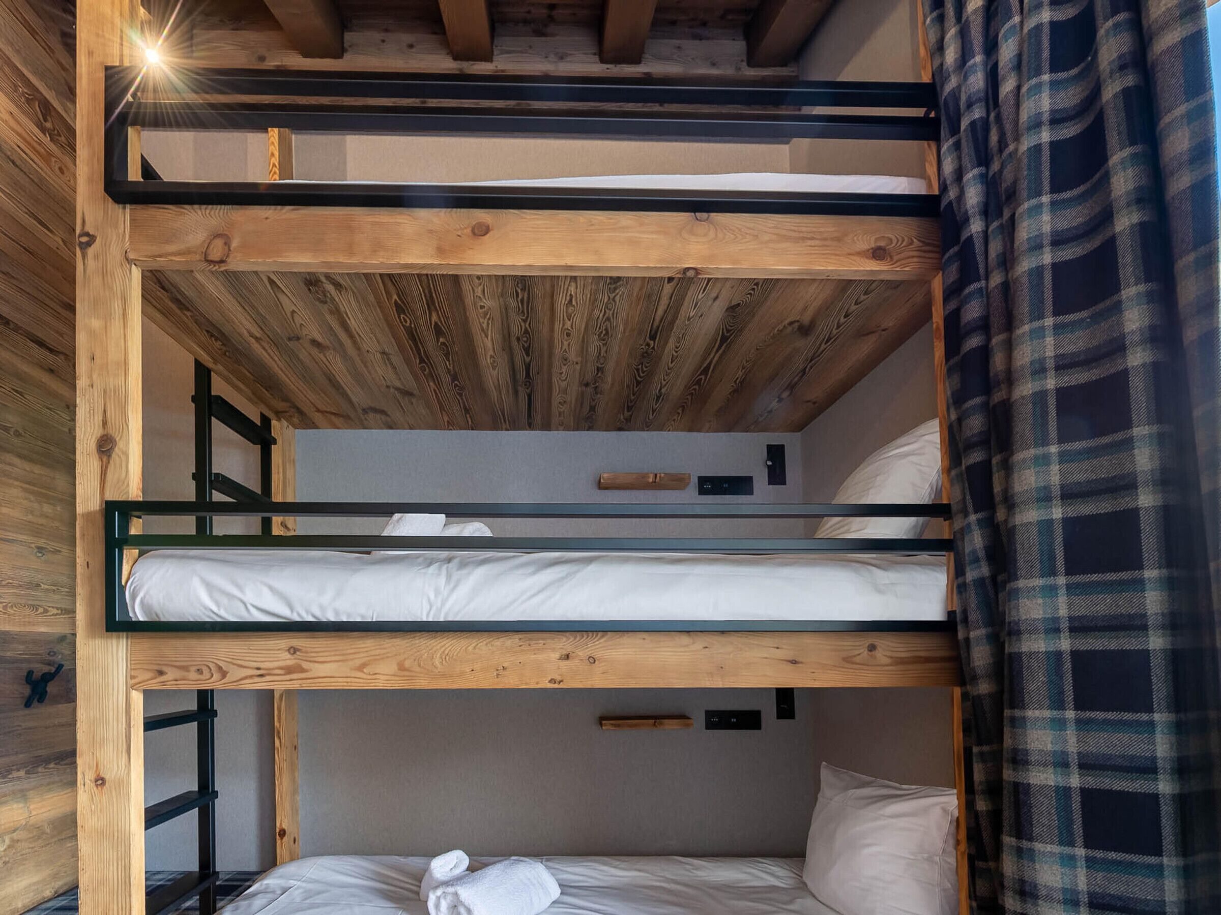 A bunk bed room with wooden beams, a ladder, and a plaid curtain.