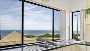 Een keuken met een groot raam dat uitkijkt over de oceaan, een spoelbak en een modern design.