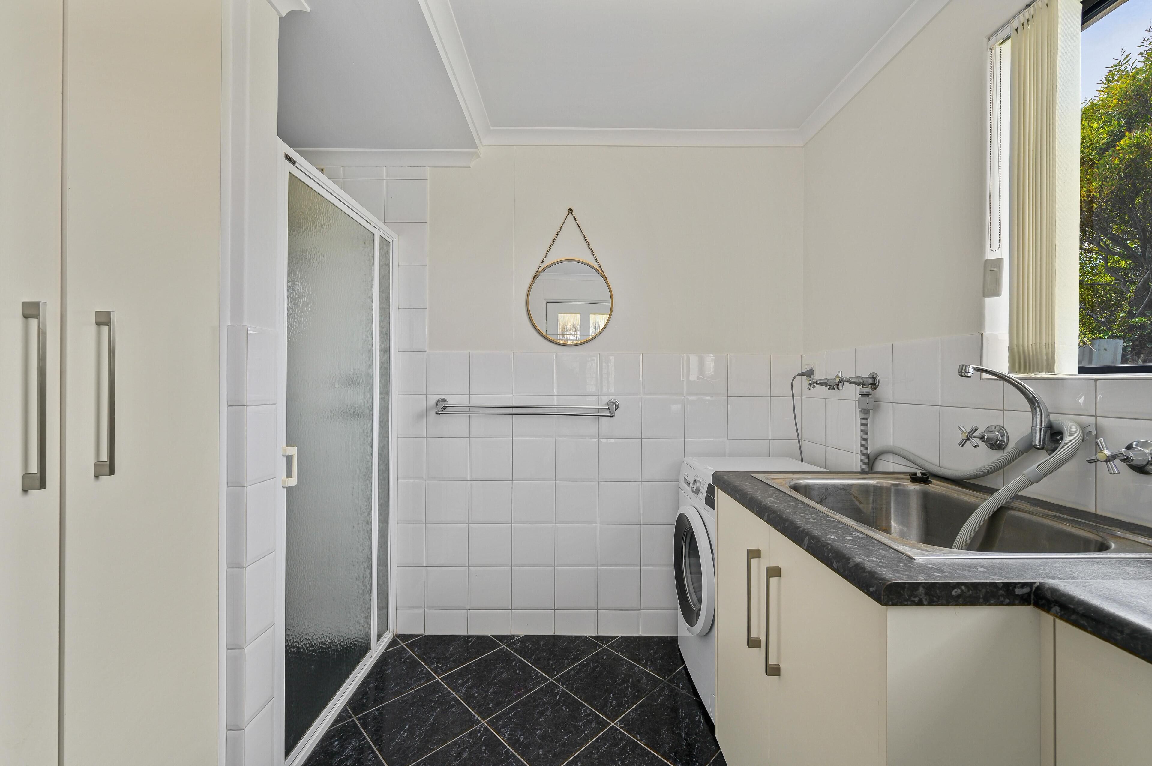 Casa de banho moderna com chuveiro, sanita, lavatório e máquina de lavar roupa.