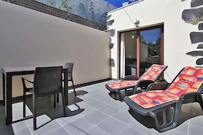 A patio with a table and chairs, a pair of sun loungers, and a sliding glass door leading to an interior space. - Bungalow Moijama 1, Puerto Naos (Puerto Naos)