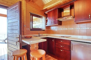 A compact kitchen with wooden cabinets, a stainless steel refrigerator, and a wooden stool. - Bungalow Moijama 7, Puerto Naos (Puerto Naos)