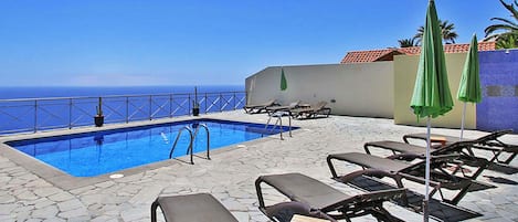 Ein Poolbereich mit Liegestühlen und Sonnenschirmen, einem strahlend blauen Himmel und Blick aufs Meer.