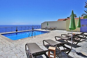 Ein Poolbereich mit Liegestühlen und Sonnenschirmen, einem strahlend blauen Himmel und Blick aufs Meer.