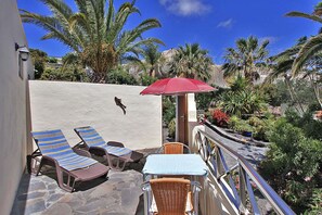 Een terras met loungestoelen, een tafel en een rode parasol.