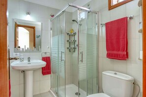 Ein Badezimmer mit einer Duschkabine, einem weißen Waschbecken und einer Toilette.