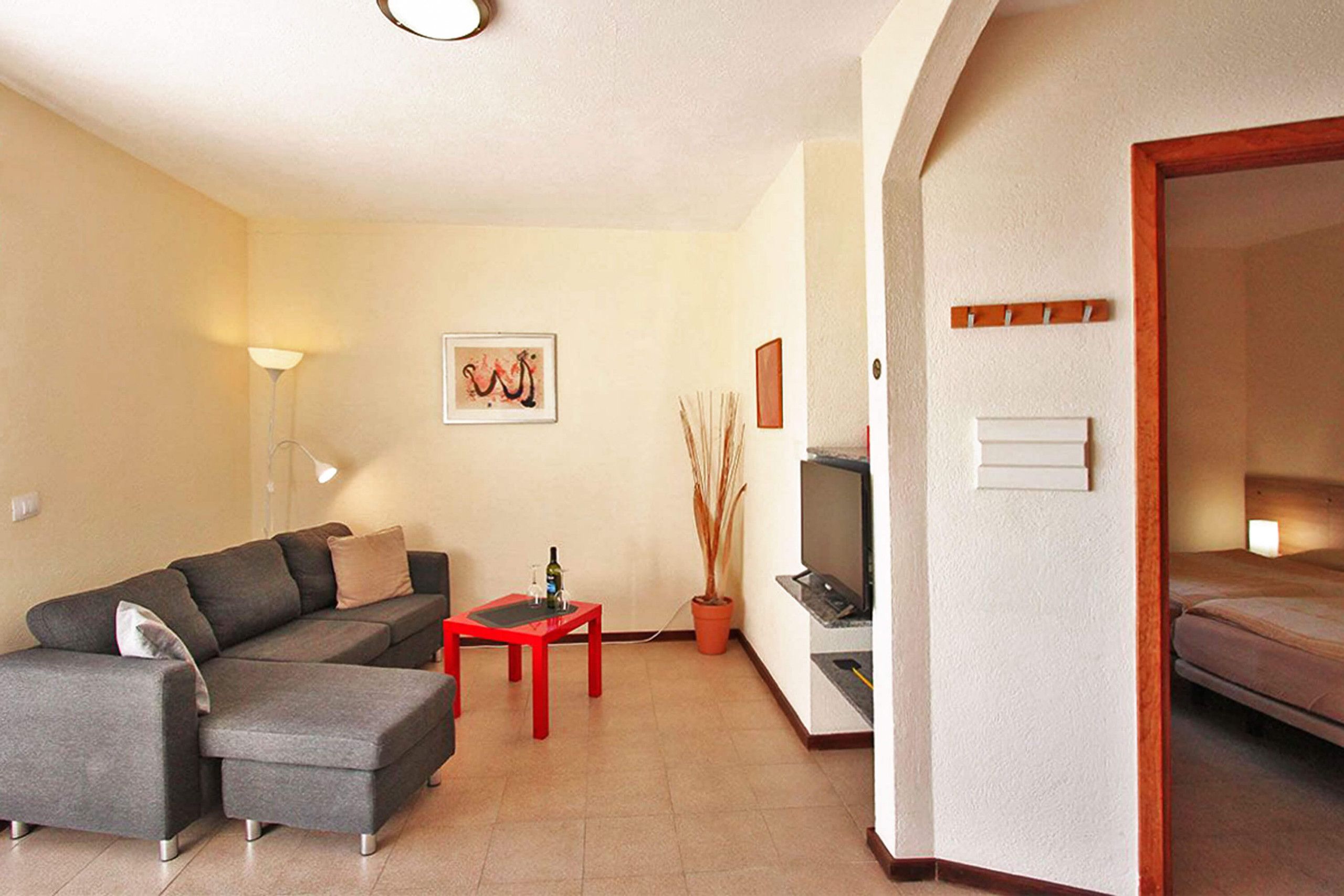A living room with a sectional sofa, a red coffee table, a TV, and a potted plant.