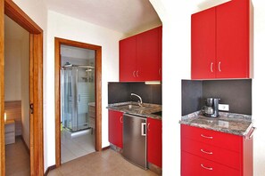 Eine kleine Küche mit roten Schränken, einem Edelstahl-Kühlschrank und einer Arbeitsplatte aus Granit.