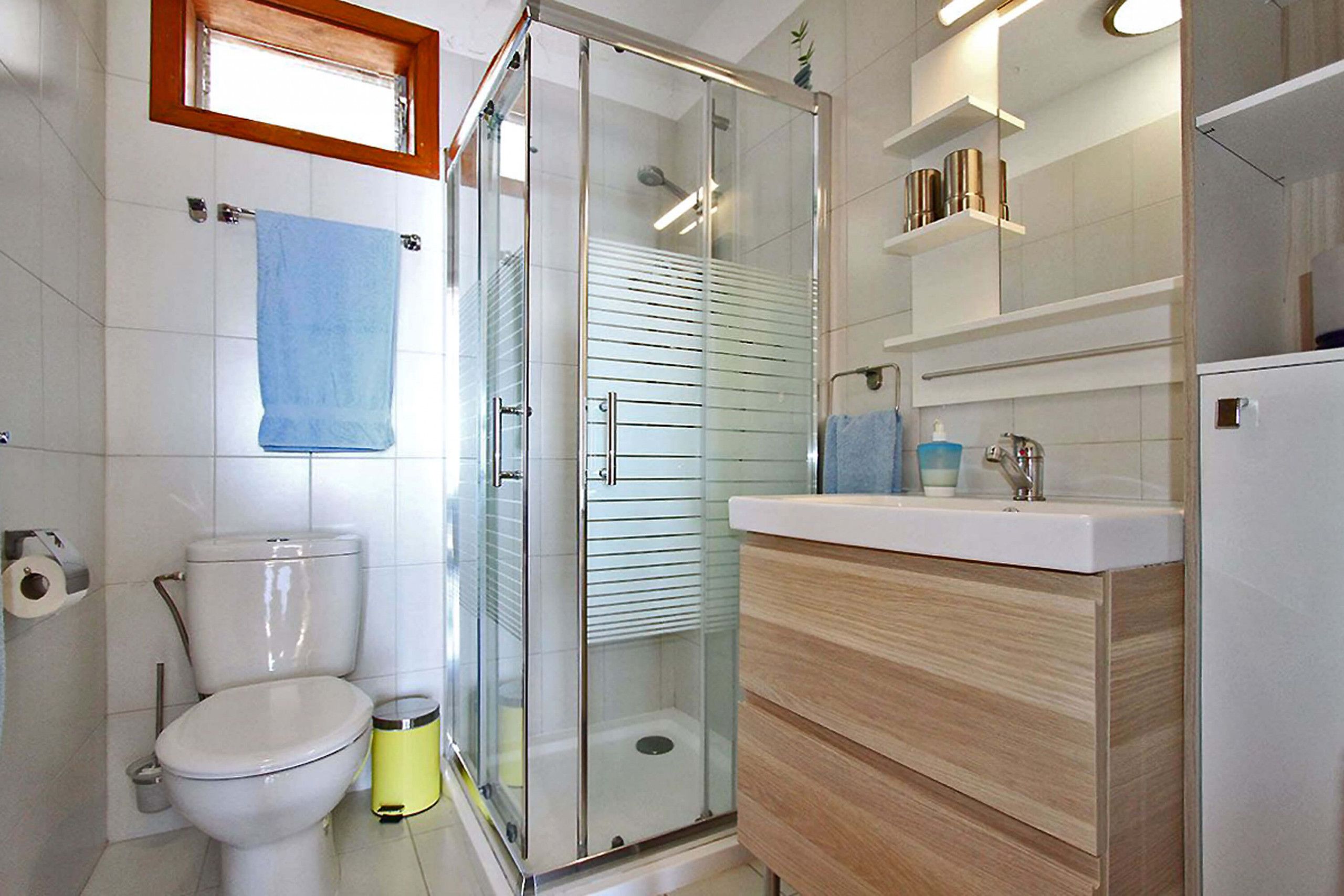 Un baño moderno con ducha de vidrio, inodoro y tocador con espejo y repisas.