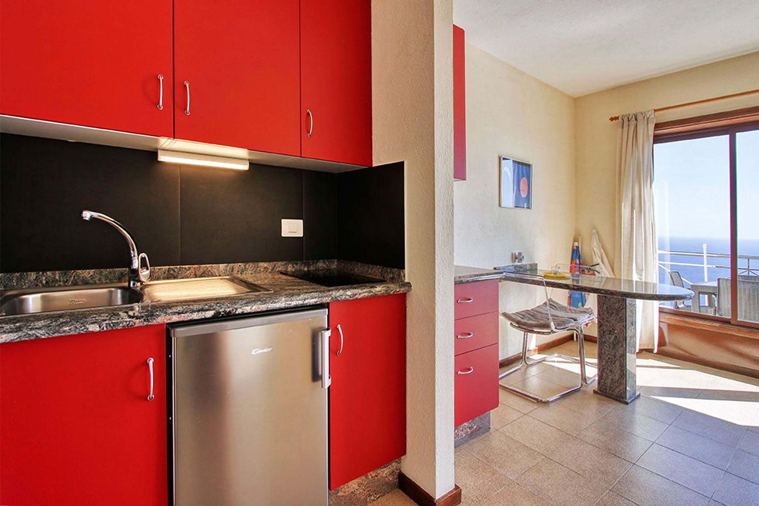 Une cuisine moderne avec des meubles rouges, des appareils en acier inoxydable et un plan de travail en marbre.