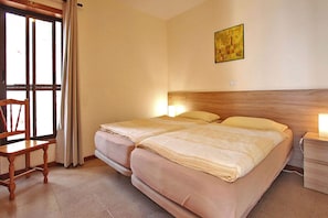 A hotel room with two beds, a wooden headboard, a chair, a window with curtains, and a painting on the wall. - Bungalow Moijama 8, Puerto Naos (Puerto Naos)