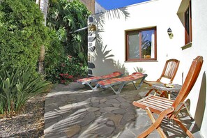 A patio with stone flooring, two wooden lounge chairs, and a small table. - Bungalow Moijama 4, en Puerto Naos (Puerto Naos)