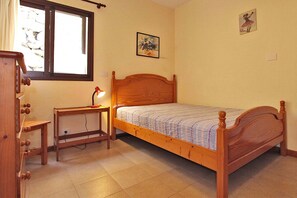 Une chambre à coucher avec un lit en bois, une table de chevet avec une lampe, une commode et une fenêtre avec des rideaux.