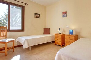 Een slaapkamer met twee eenpersoonsbedden, een houten dressoir, een stoel en een raam met uitzicht op palmbomen.