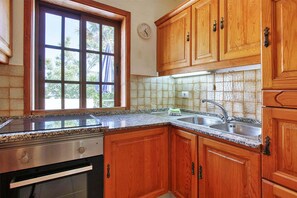 Une cuisine avec des meubles en bois, une cuisinière en acier inoxydable, une fenêtre et un dosseret carrelé.