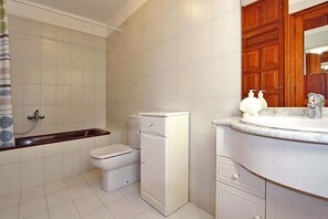 Un baño con inodoro, un armario blanco pequeño, un lavabo con espejo y zona de ducha.