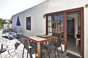 Un patio al aire libre con una mesa y sillas de madera, un paraguas azul y sillas de lounge.