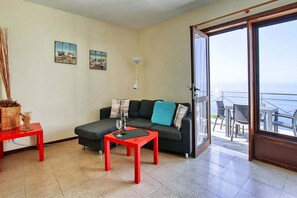A living room with a sofa, a red table, and a balcony with outdoor furniture. - Bungalow Moijama 10, en Puerto Naos (Puerto Naos)