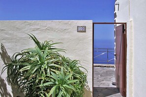 Ein weißes Gebäude mit der Hausnummer 10, einem Blumentopf und Blick auf das Meer durch ein Tor.