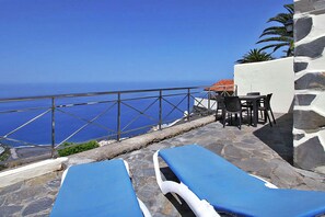 A terrace with stone flooring, two blue lounge chairs, a table with chairs, and a view of the sea. - Bungalow Moijama 10, en Puerto Naos (Puerto Naos)