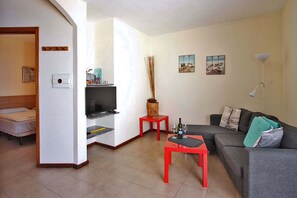 A compact living space with a bed, a TV, a sofa, and a small table with a bottle and glasses. - Bungalow Moijama 10, en Puerto Naos (Puerto Naos)