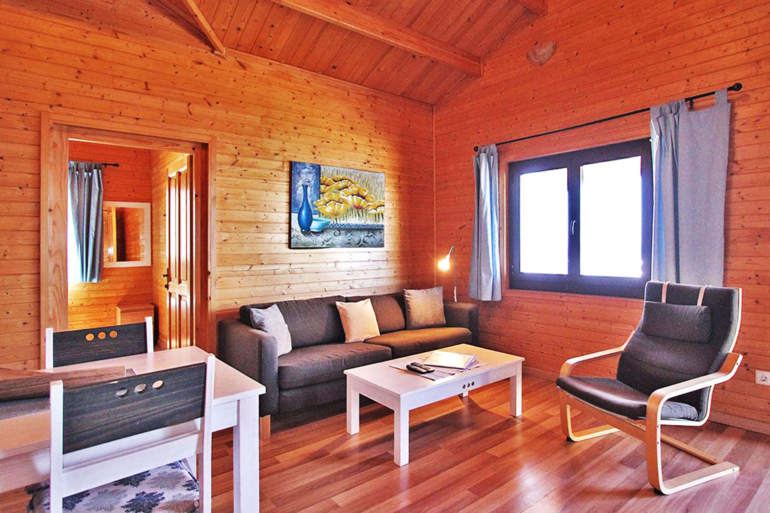 Een houten chalet van binnen met een bank, salontafel en een schommelstoel.