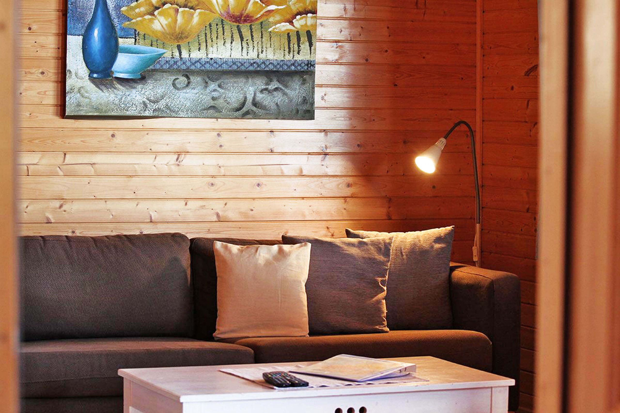 A cozy living room with a wooden wall, a brown sofa, and a white coffee table with a remote control and papers.