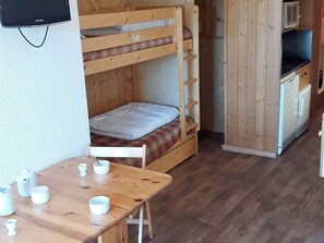 Un lit superposé avec une table en bois et des tasses blanches, un four à micro-ondes et un réfrigérateur, le tout dans une pièce aux murs en bois.