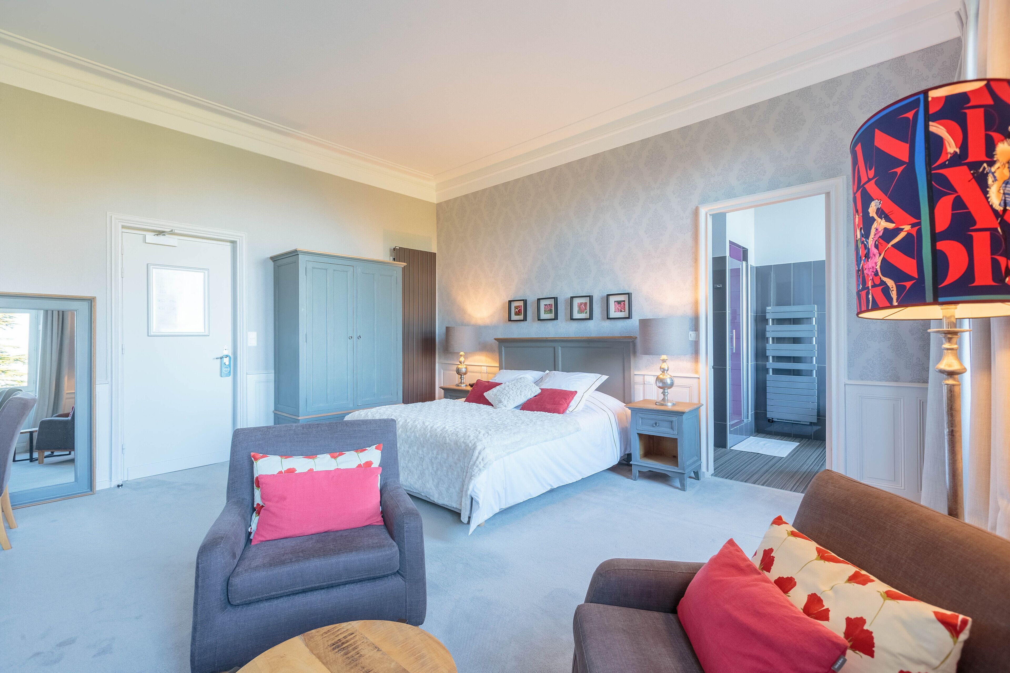 A bedroom with a bed, two armchairs, a nightstand, and a lamp.