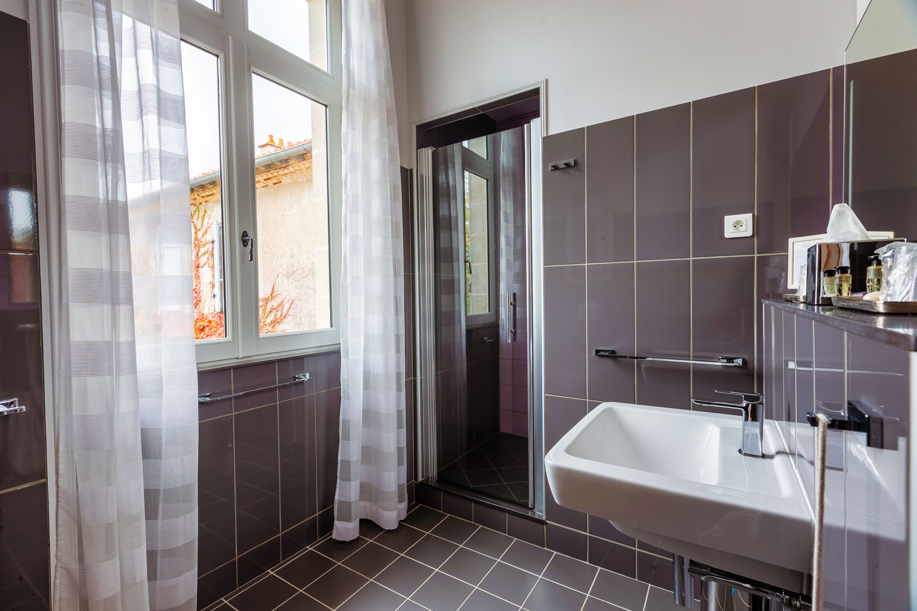 A modern bathroom with a shower, a sink, and a window with curtains.