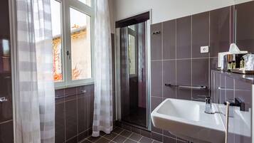 A modern bathroom with a shower, a sink, and a window with curtains.