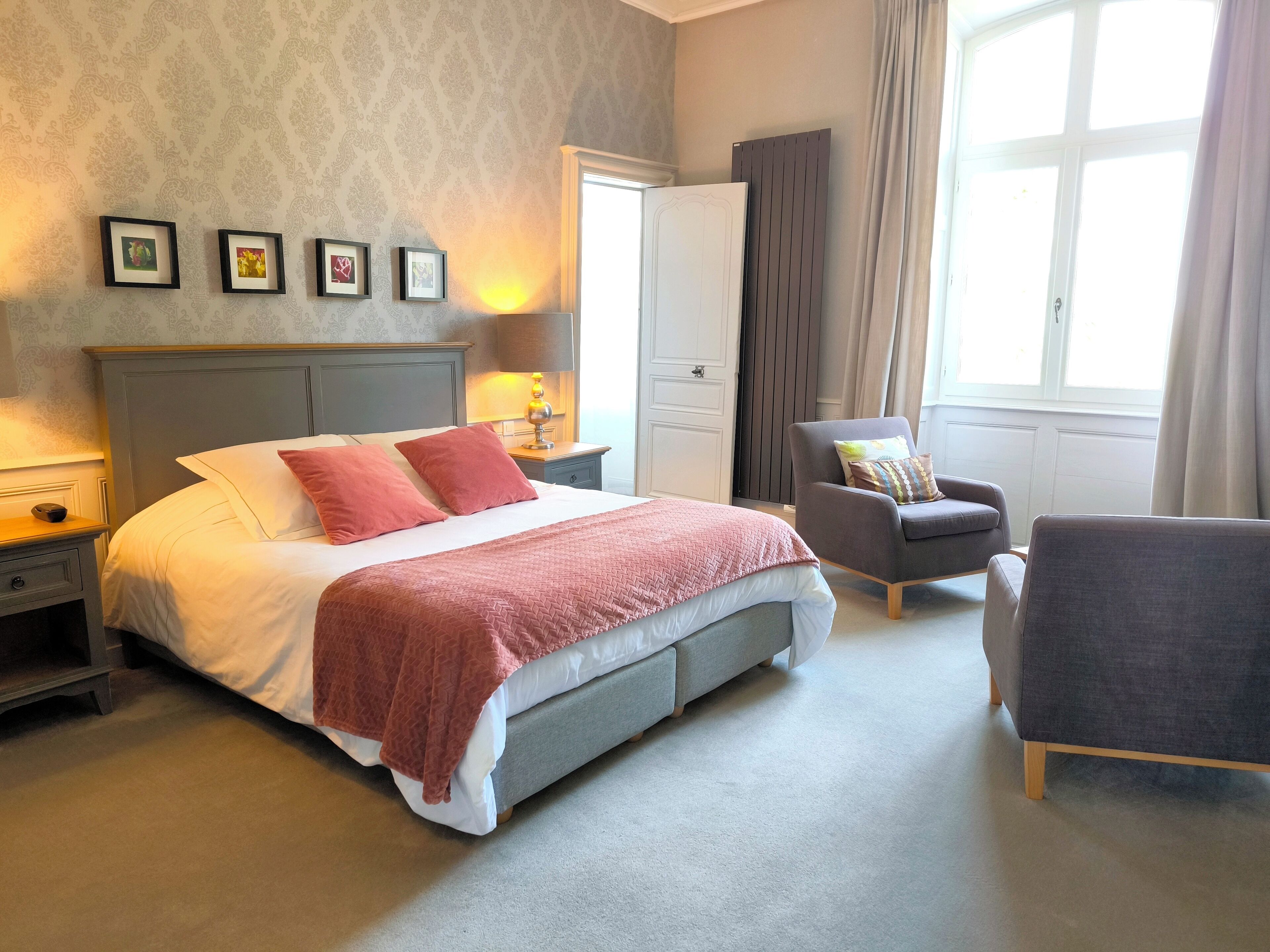Habitación de hotel con una cama grande, una silla, una mesita de noche, una lámpara y una ventana con cortinas.