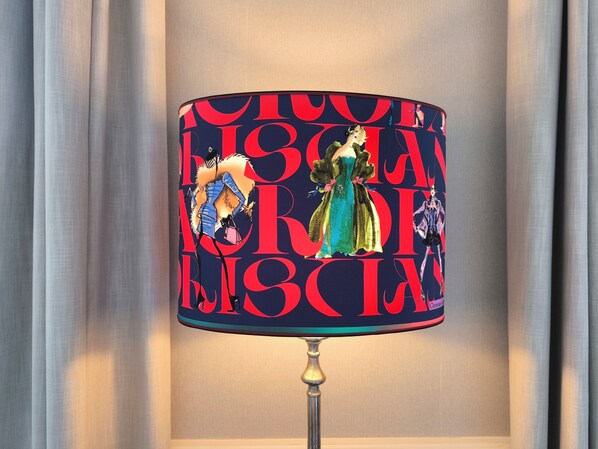 A lamp with a decorative cover featuring abstract figures and bold text.
