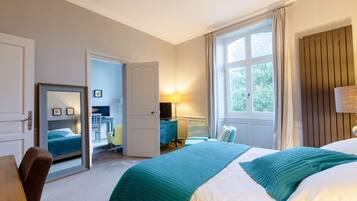 Una habitación de hotel con cama, escritorio, silla, lámpara y ventana con cortinas.
