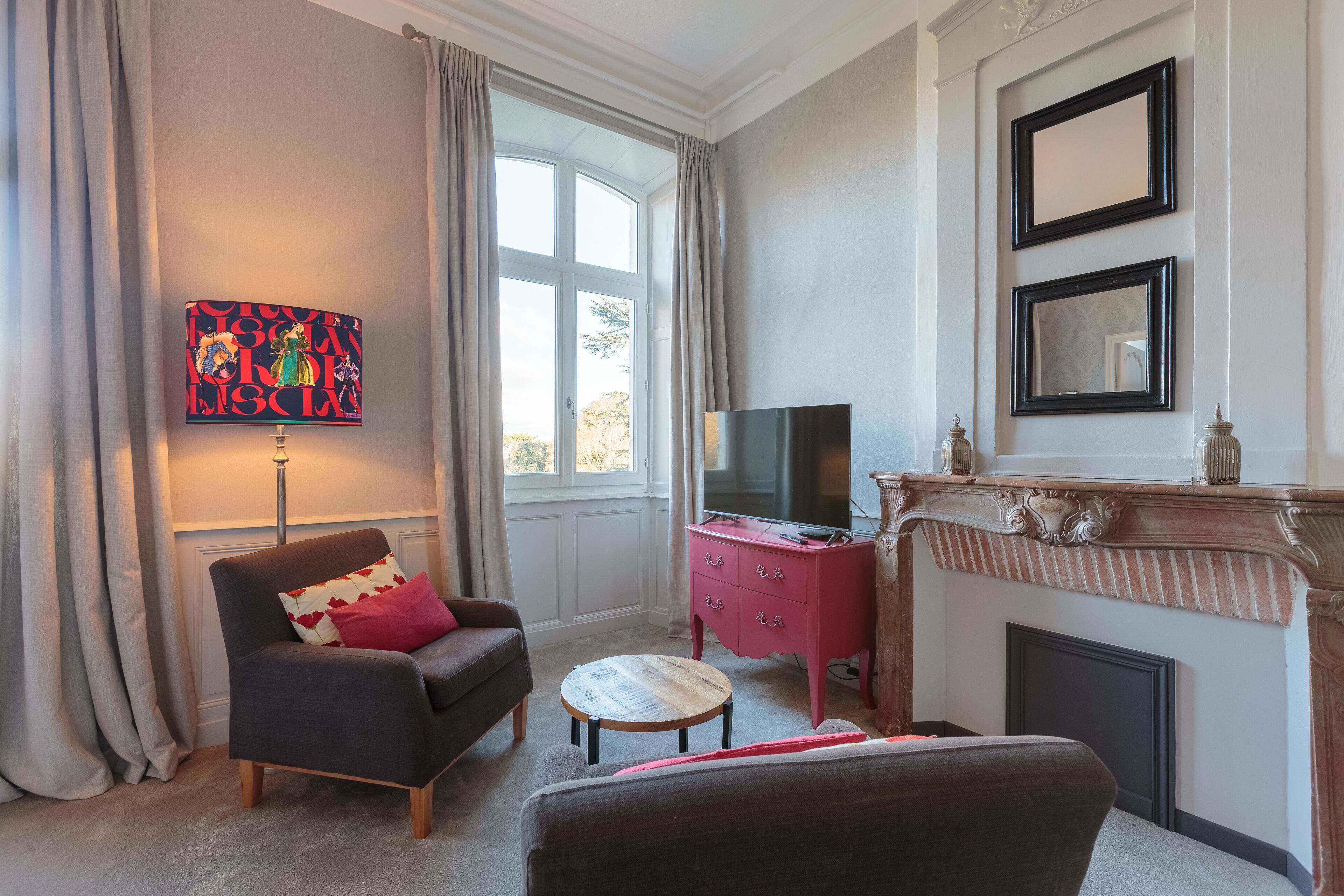 A living room with a sofa, a small round table, a TV, a fireplace, and a painting on the wall.