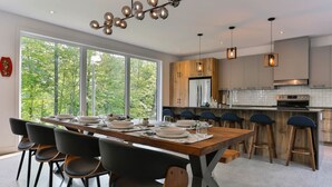 A modern kitchen with a wooden island, bar stools, and a large dining table with chairs. - New Family Cottage Tremblant-4 Bdrs w/ Hot Tub (La Conception)