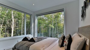 A bedroom with a large bed, two windows, and a view of trees. - New Family Cottage Tremblant-4 Bdrs w/ Hot Tub (La Conception)