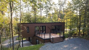 A modern wooden cabin with a deck, surrounded by trees. - New Family Cottage Tremblant-4 Bdrs w/ Hot Tub (La Conception)