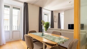 Een eetgedeelte met een houten tafel, vier stoelen, een vaas met een plant en een bank op de achtergrond.
