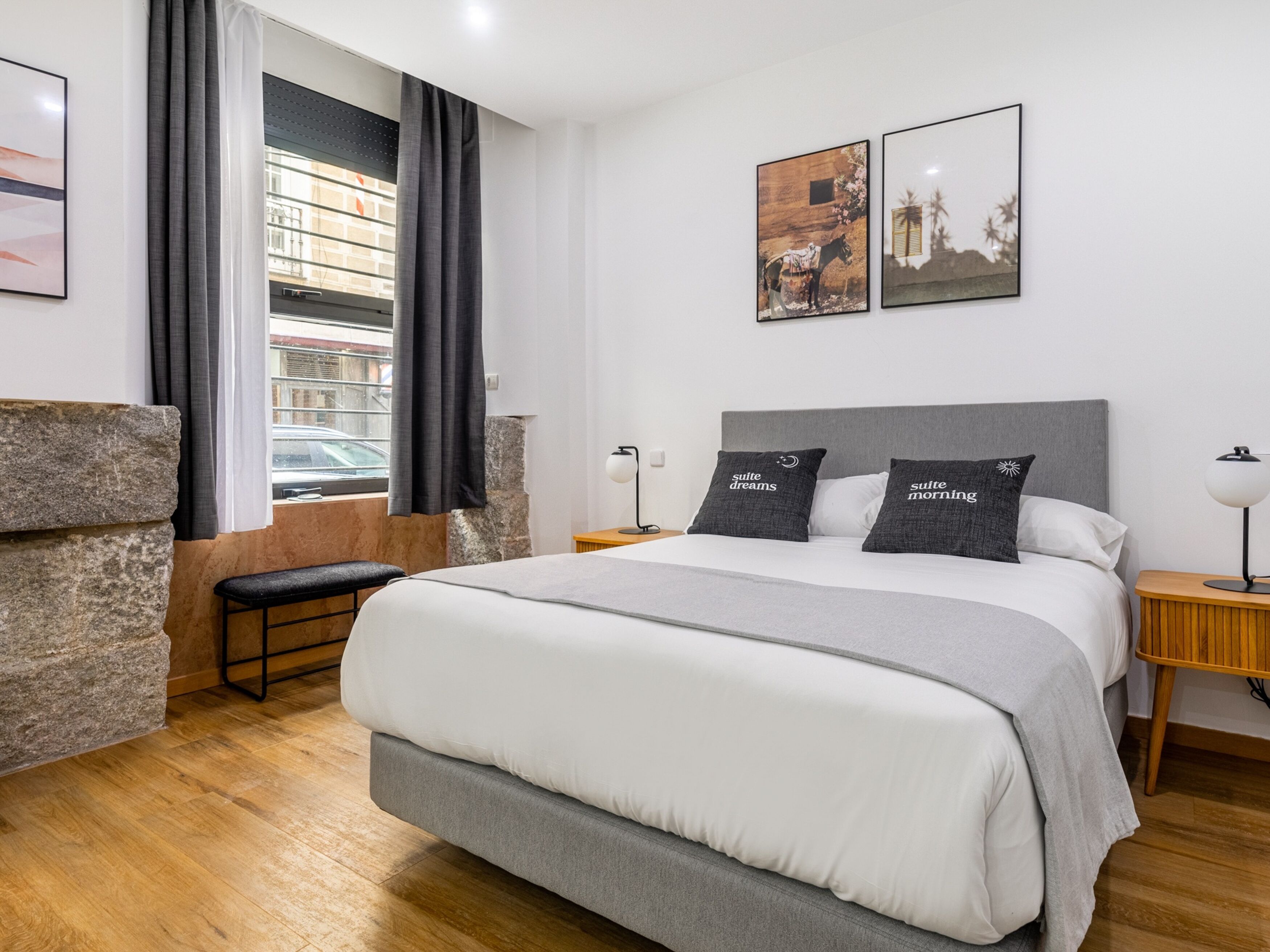 Een moderne slaapkamer met een groot bed, een bankje, een nachtkastje en twee afbeeldingen in lijsten aan de muur.