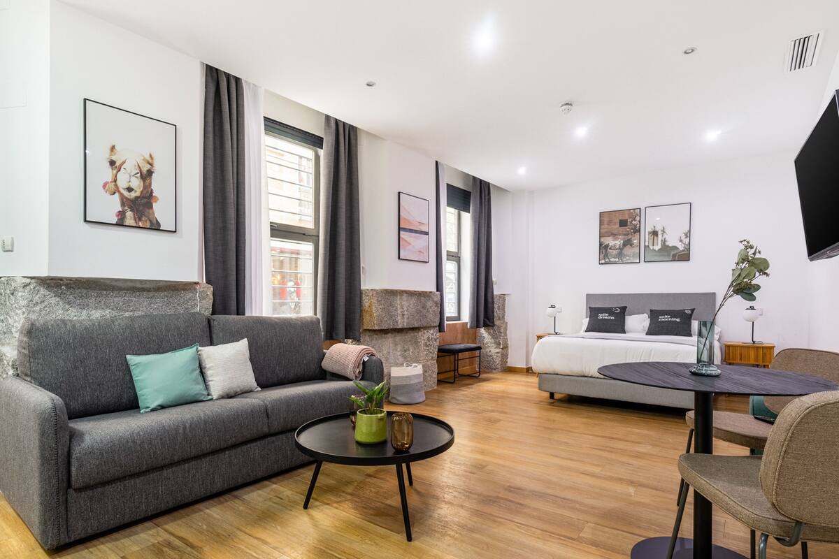 Ein modernes Wohnzimmer mit einem grauen Sofa, einem runden Couchtisch mit einer Pflanze und einem Essbereich mit Tisch und Stühlen.