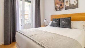 Hotelkamer met een groot bed, grijze gordijnen, een houten hoofdbord en twee aan de muur bevestigde foto's.