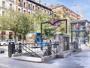 Eine Metrostation mit Bushaltestelle und Fußgängerüberweg, sowie ein Gebäude mit dem Schriftzug 'Tribunal'.