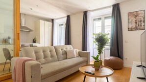 Een moderne woonkamer met een beige bank, een ronde houten salontafel, een potplant en een rond zitkussen.