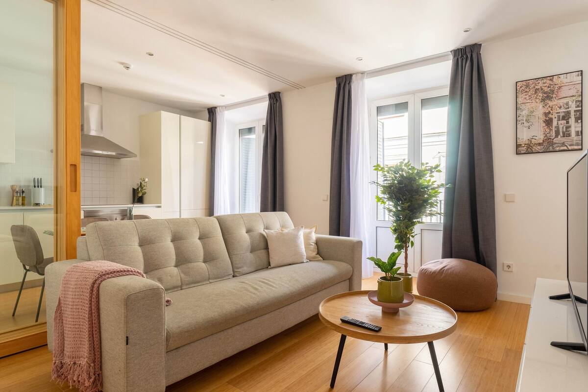 Ein modernes Wohnzimmer mit einem beigen Sofa, einem runden Holztisch, einer Topfpflanze und einem runden Hocker.