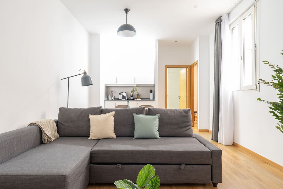 Ein modernes Wohnzimmer mit einem grauen Ecksofa, einer Stehlampe und einem Blumentopf.