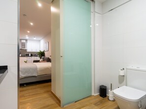 Ein kleines Hotelzimmer mit einem Bett, einer Kochnische und einem Badezimmer inklusive Toilette und Mülleimer.